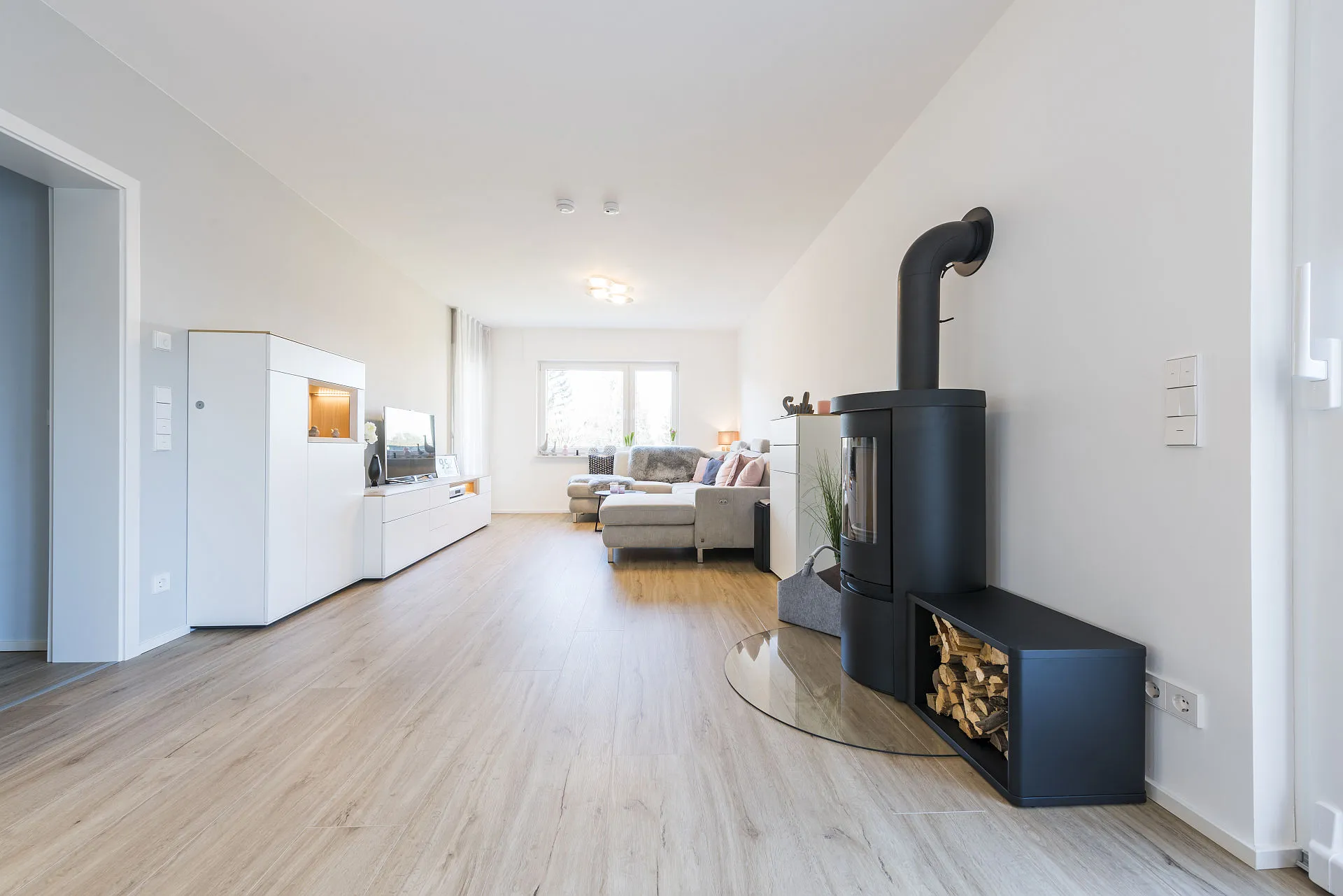 Heller Wohnraum mit Holzboden, schwarzen Kamin, weißen Möbeln und Fenster.