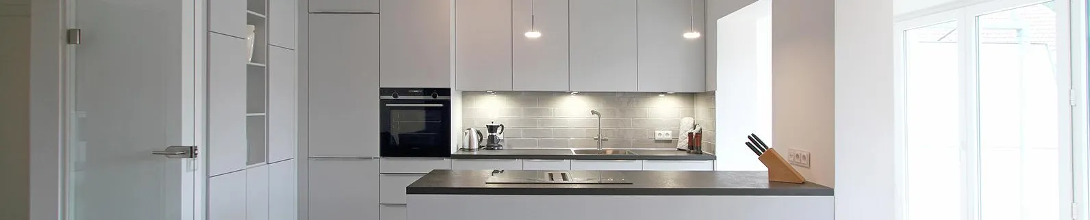 Moderne Einbauküche in einer Ferienwohnung mit klaren Linien und minimalistischer Ästhetik. Helle Fronten, dezente Beleuchtung und eine praktische Arbeitsinsel sorgen für Funktionalität und stilvolles Design in einem einladenden Ambiente.