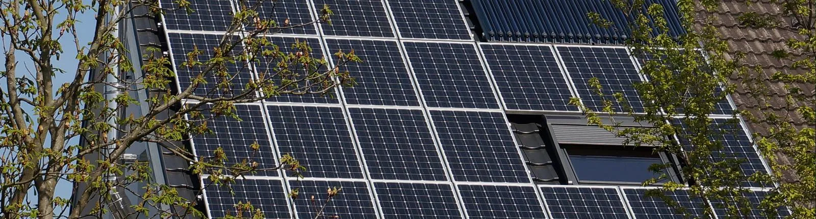 Großaufnahme eines Daches mit zahlreichen Solarpanels und einem zusätzlichen Solarthermie-Element zur Warmwasserbereitung. 