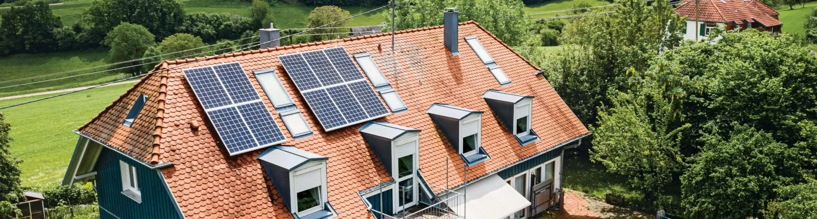 Luftaufnahme eines Hauses mit rotem Ziegeldach, auf dem mehrere Solarpanels installiert sind.