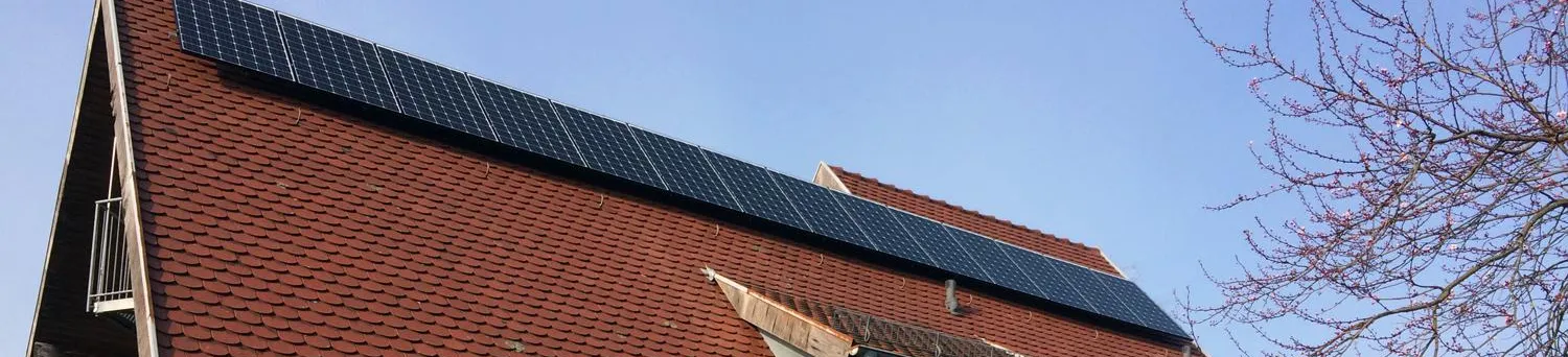 Ein Haus mit schrägem, roten Ziegeldach, auf dem mehrere Solarpanels installiert sind. 