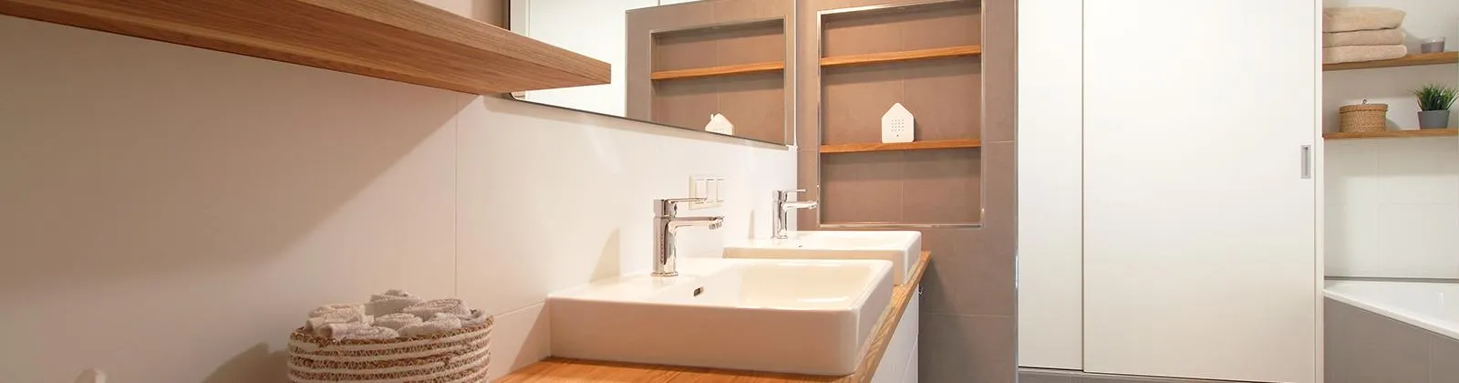 Ein modernes Badezimmer mit zwei rechteckigen Waschbecken auf einer Holzarbeitsplatte und glänzenden Armaturen. 