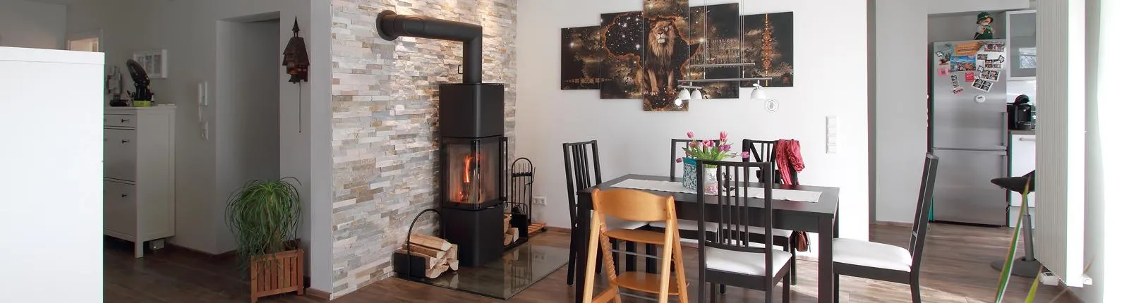 Gemütliches Wohnzimmer mit Kaminofen, dekorativer Steinwand und Essbereich, ergänzt durch warme Holzakzente und moderne Kunst an der Wand.