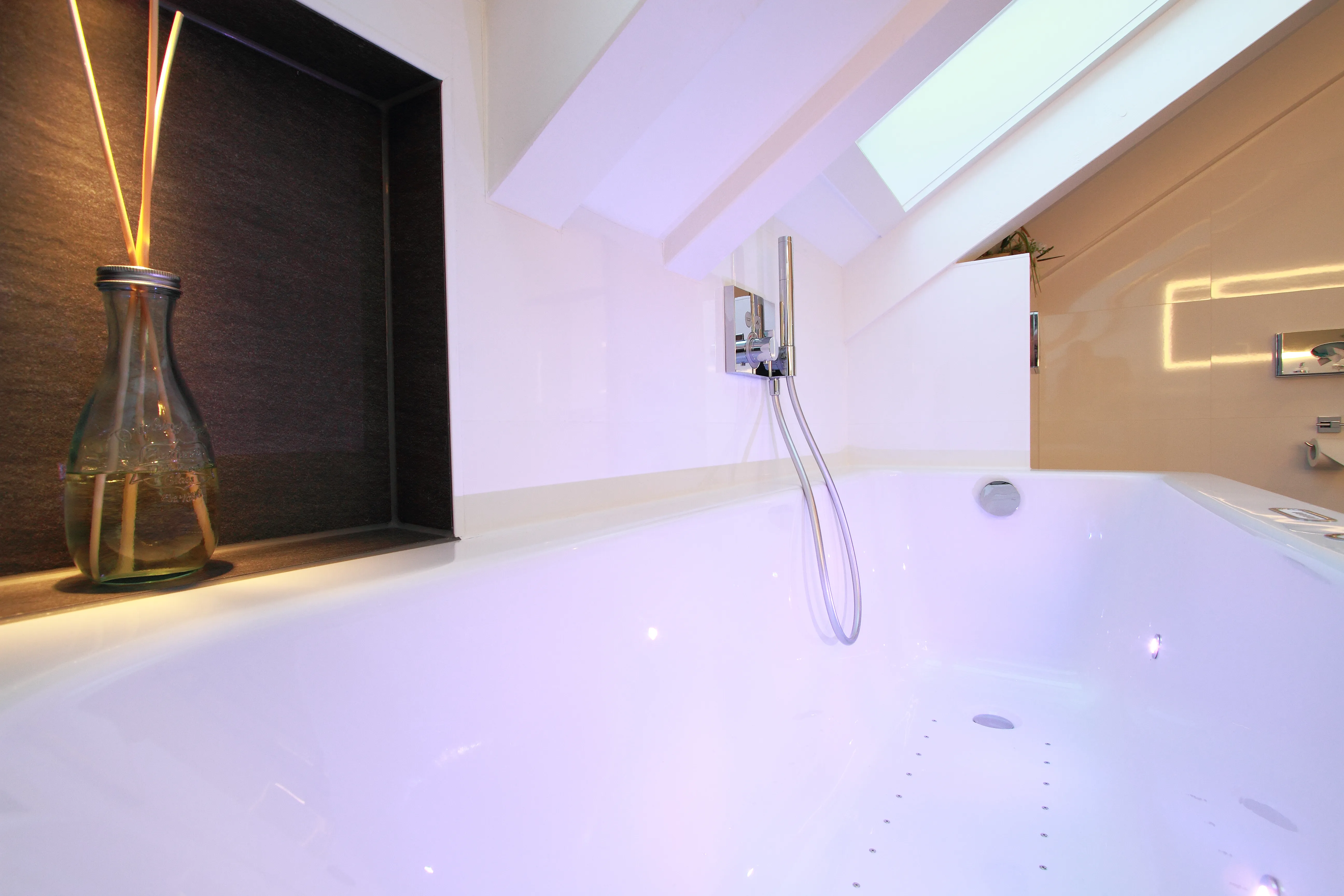 Ein luxuriöses Badezimmer mit einer freistehenden weißen Badewanne, die unter einer schrägen Decke platziert ist. 