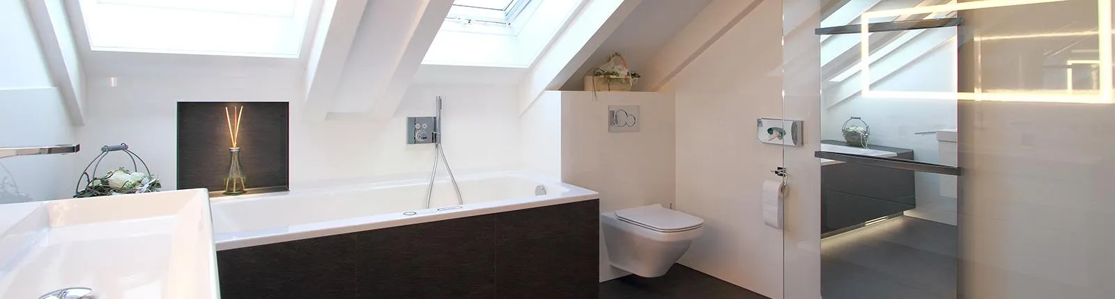 Ein modernes Badezimmer unter einer Dachschräge mit einer großzügigen Badewanne und einem Fenster, das Tageslicht hereinlässt.