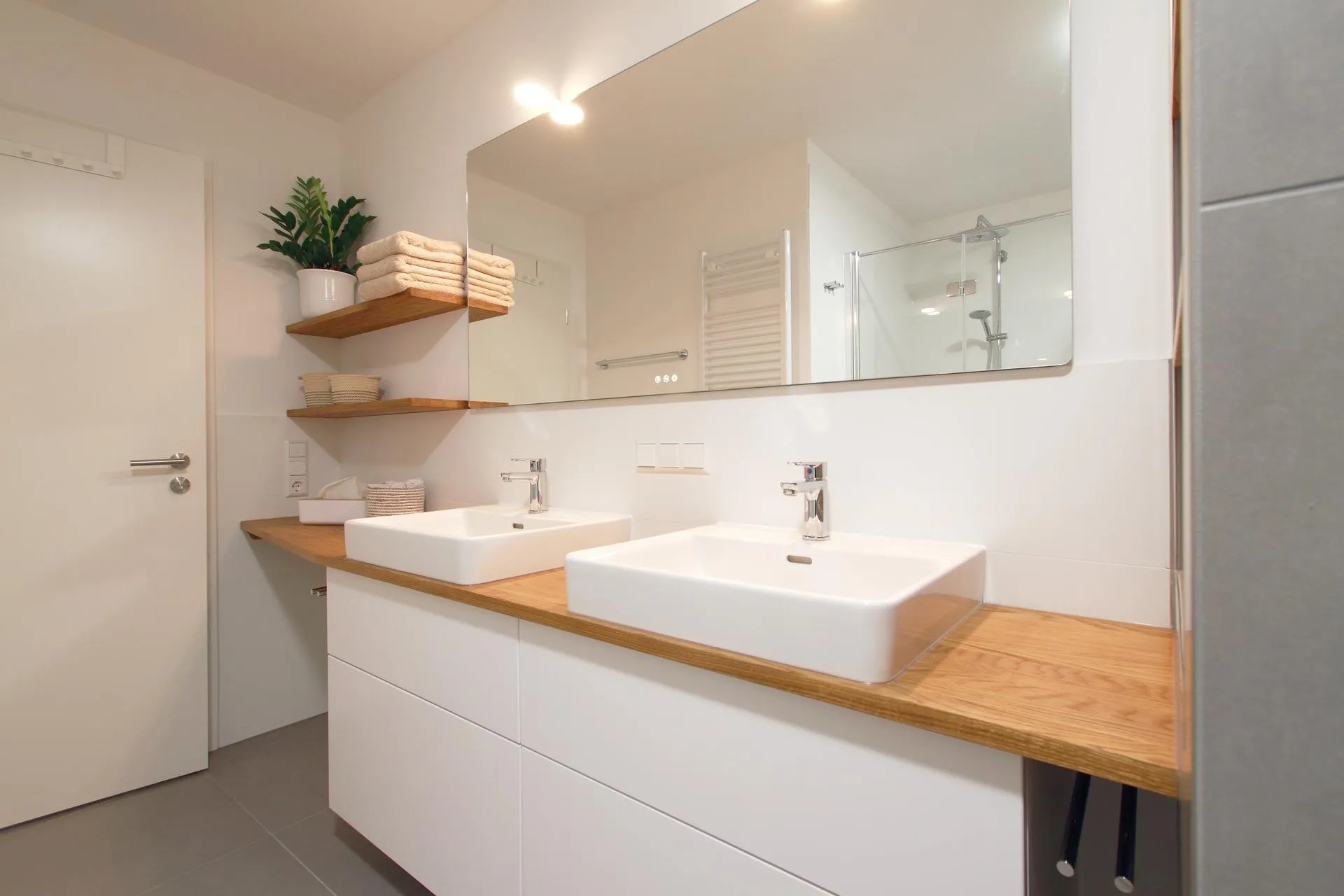 Modernes Badezimmer mit Doppelwaschtisch, Holzarbeitsplatte und großzügigem Spiegel. 