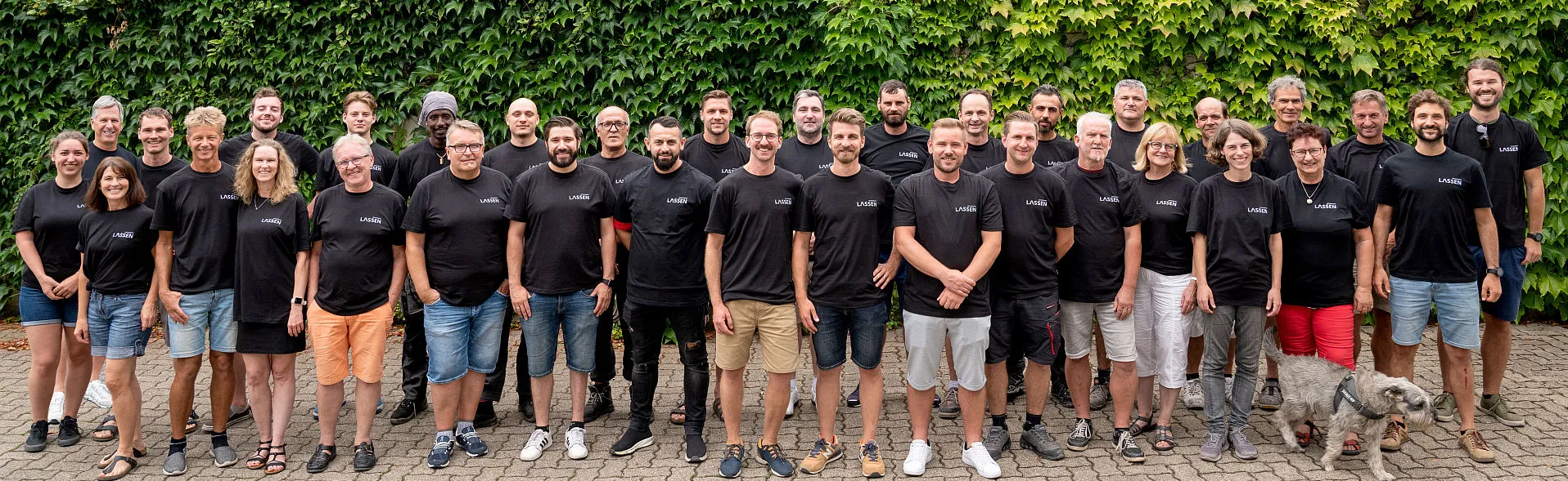 Handwerksteam der Lassen GmbH vor einer bewachsenen Mauer.