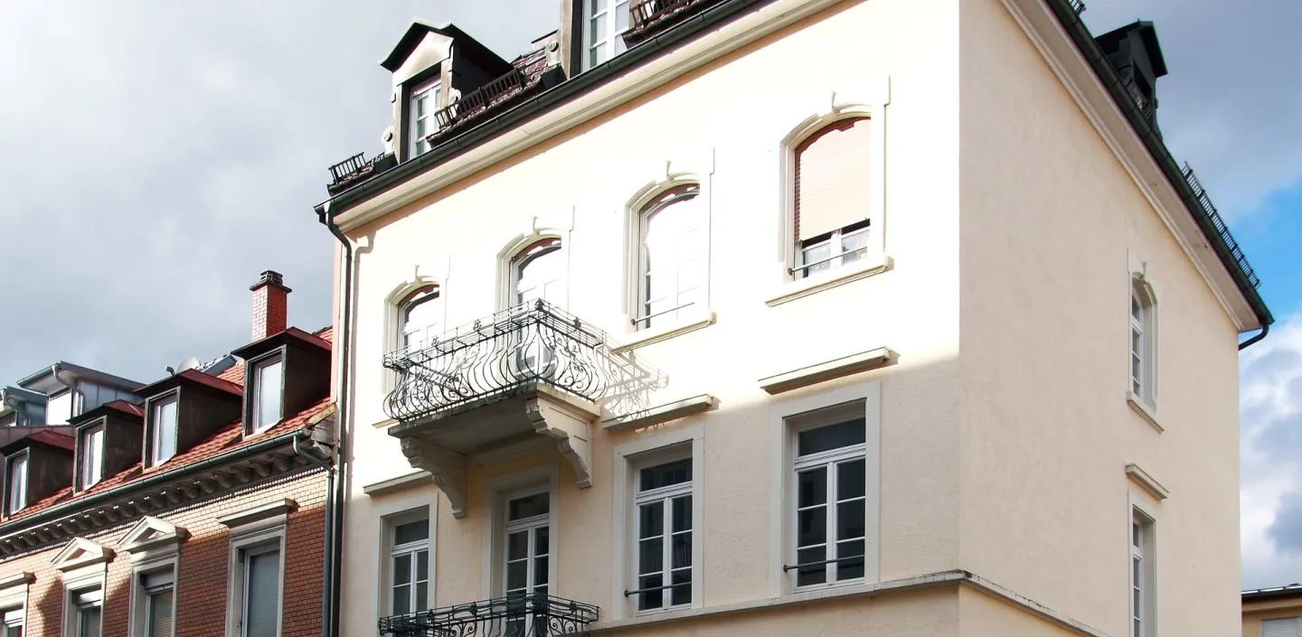 Ein elegantes, mehrstöckiges Wohngebäude mit cremefarbener Fassade und klassischen Balkongeländern. 