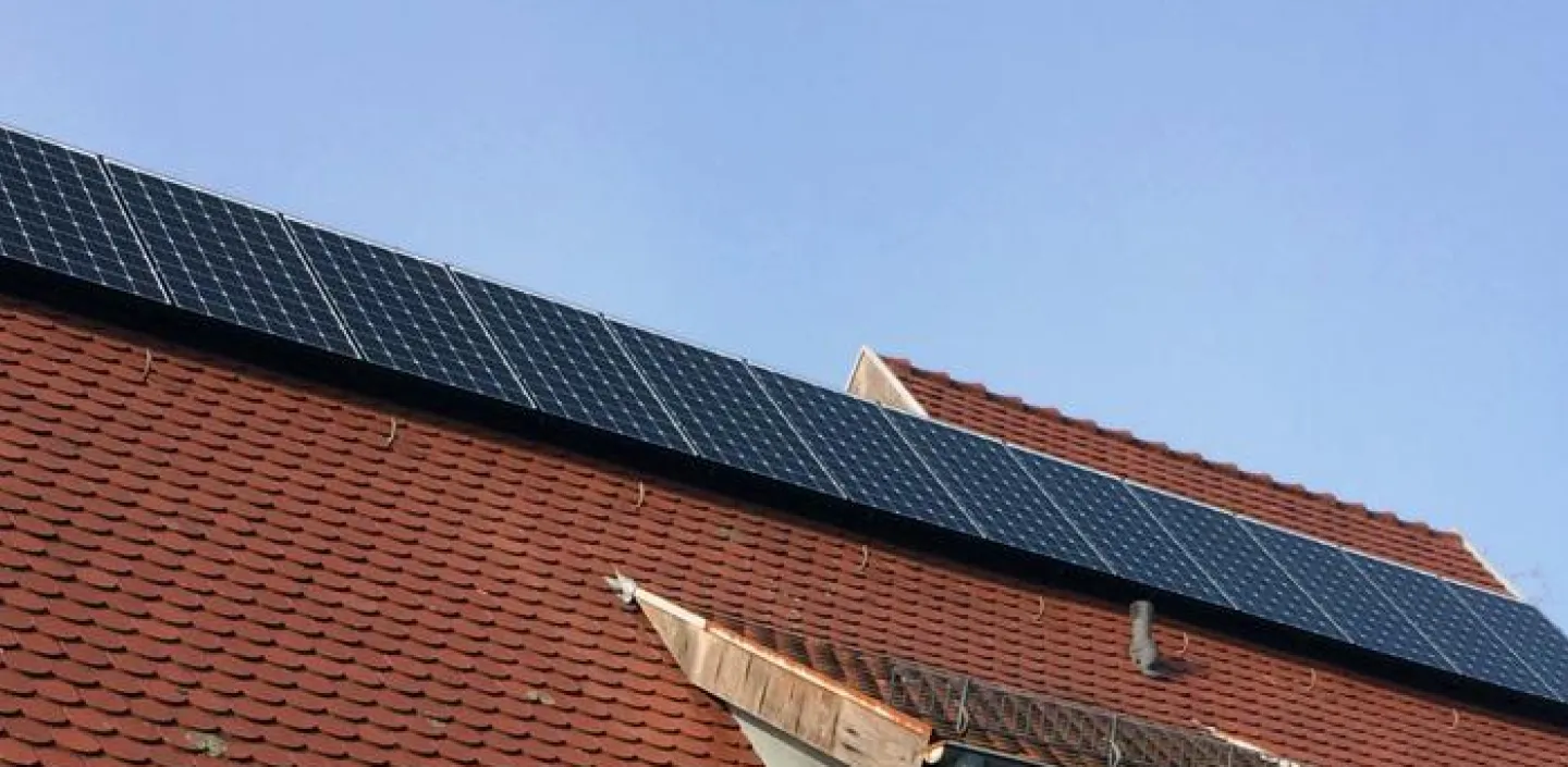 Ein Haus mit schrägem, roten Ziegeldach, auf dem mehrere Solarpanels installiert sind. 