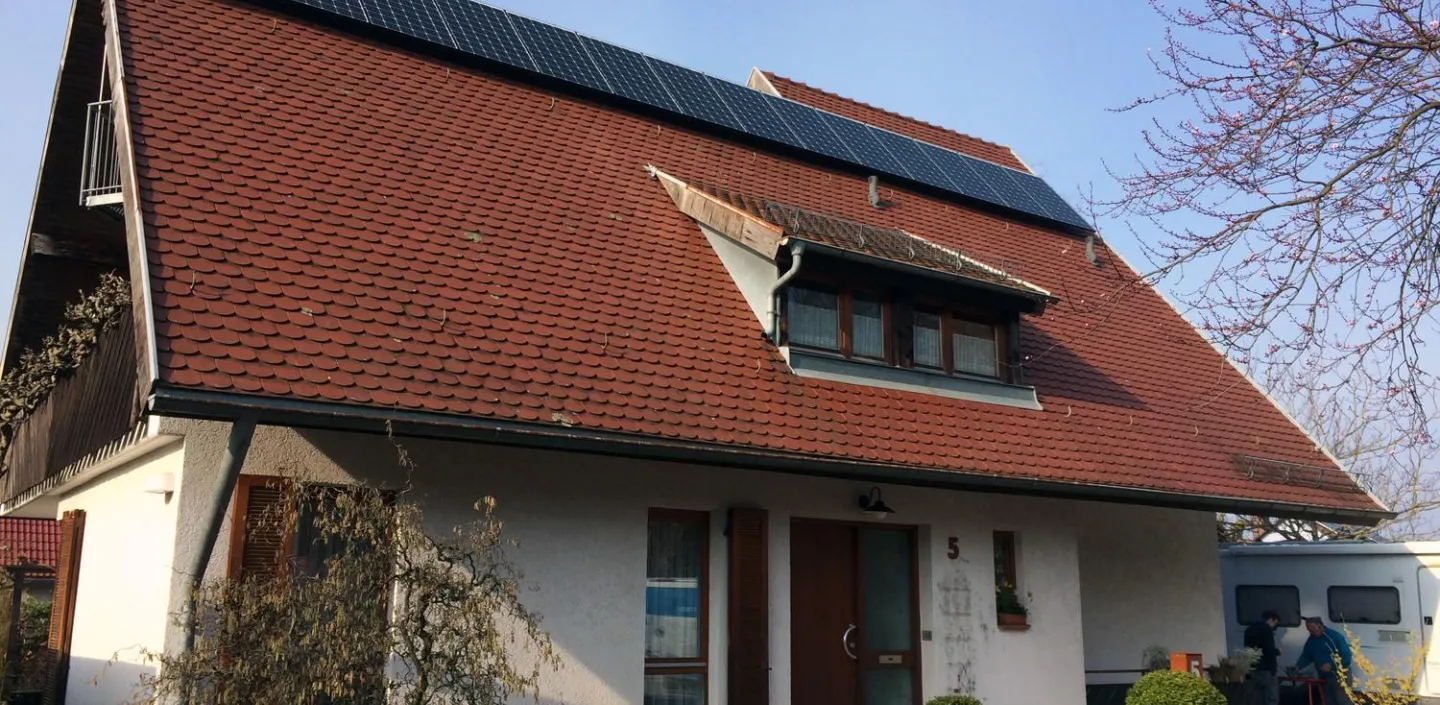 Ein Haus mit schrägem, roten Ziegeldach, auf dem mehrere Solarpanels installiert sind. 