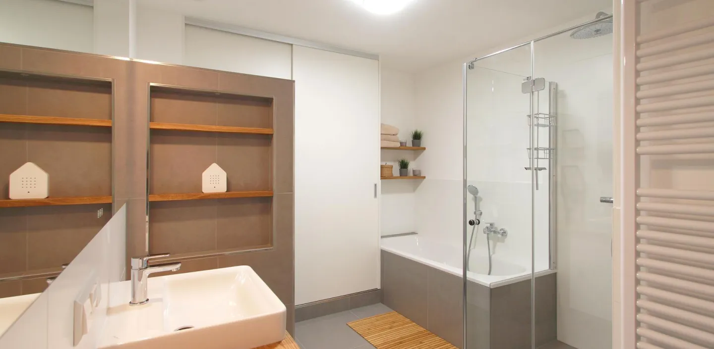 Ein modernes Badezimmer mit Doppelwaschbecken auf einer Holzplatte und großen Spiegeln, die die Raumtiefe betonen.