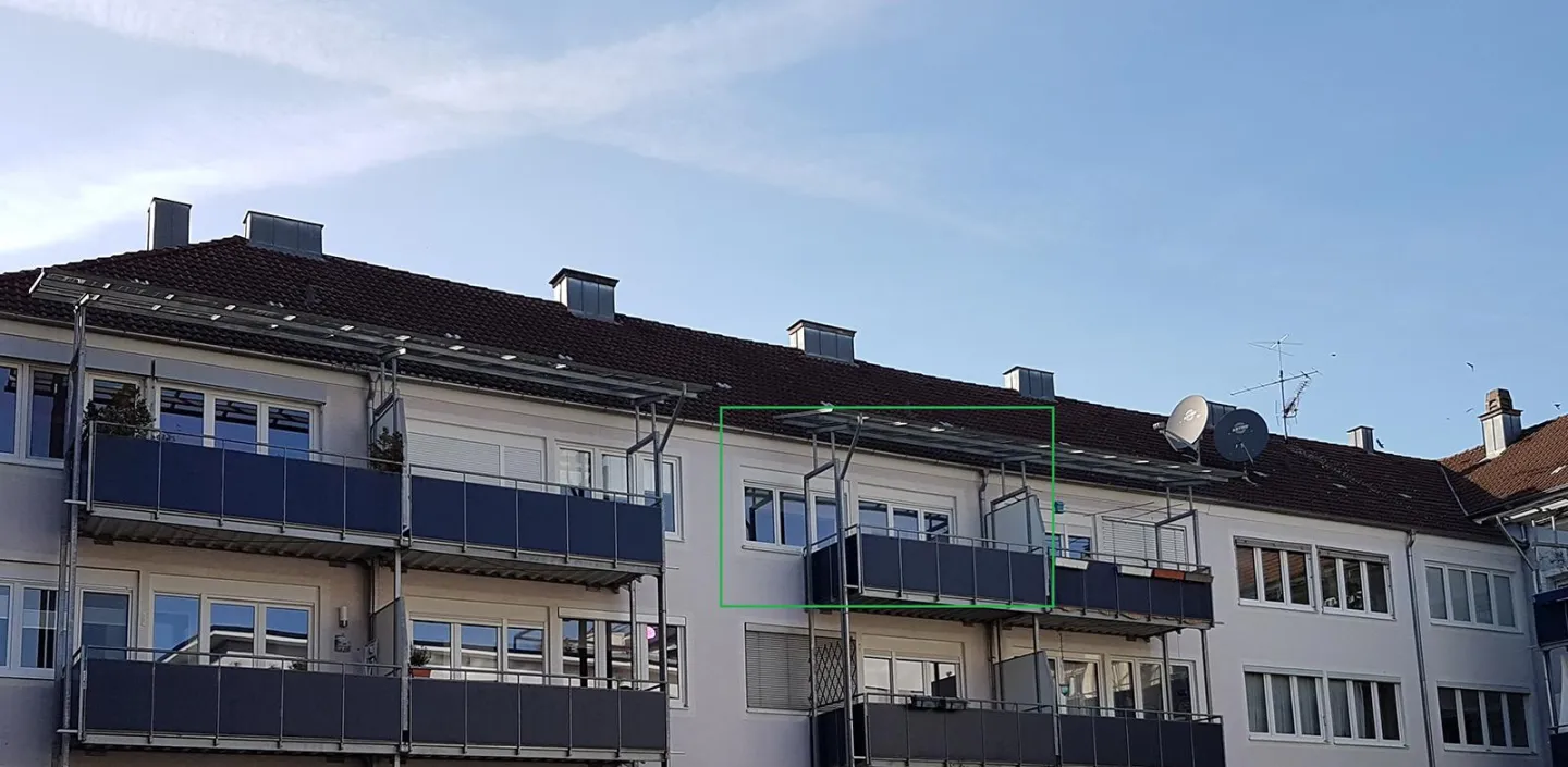 Außenansicht eines Mehrfamilienhauses mit Balkonen und moderner Fassadengestaltung. Die Balkone sind mit dunkelblauen Brüstungen und teilweise mit Überdachungen ausgestattet, die für zusätzlichen Komfort sorgen. Das Gebäude zeigt eine zeitgemäße Architektur und fügt sich harmonisch in die Umgebung ein.