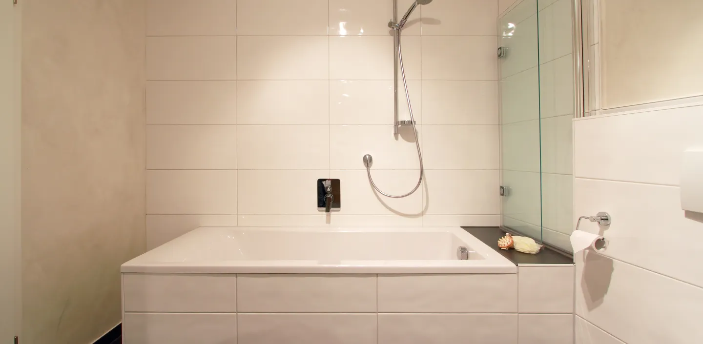 Ein modernes Badezimmer mit einer rechteckigen, in Weiß gefliesten Badewanne, die von schlichten, cremefarbenen Wänden umgeben ist.