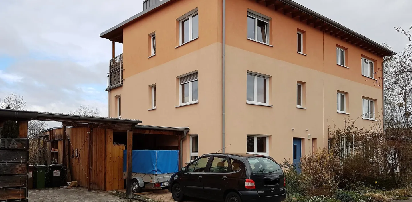 Ein dreistöckiges Mehrfamilienhaus mit orangefarbener Fassade und einem flach geneigten Dach.