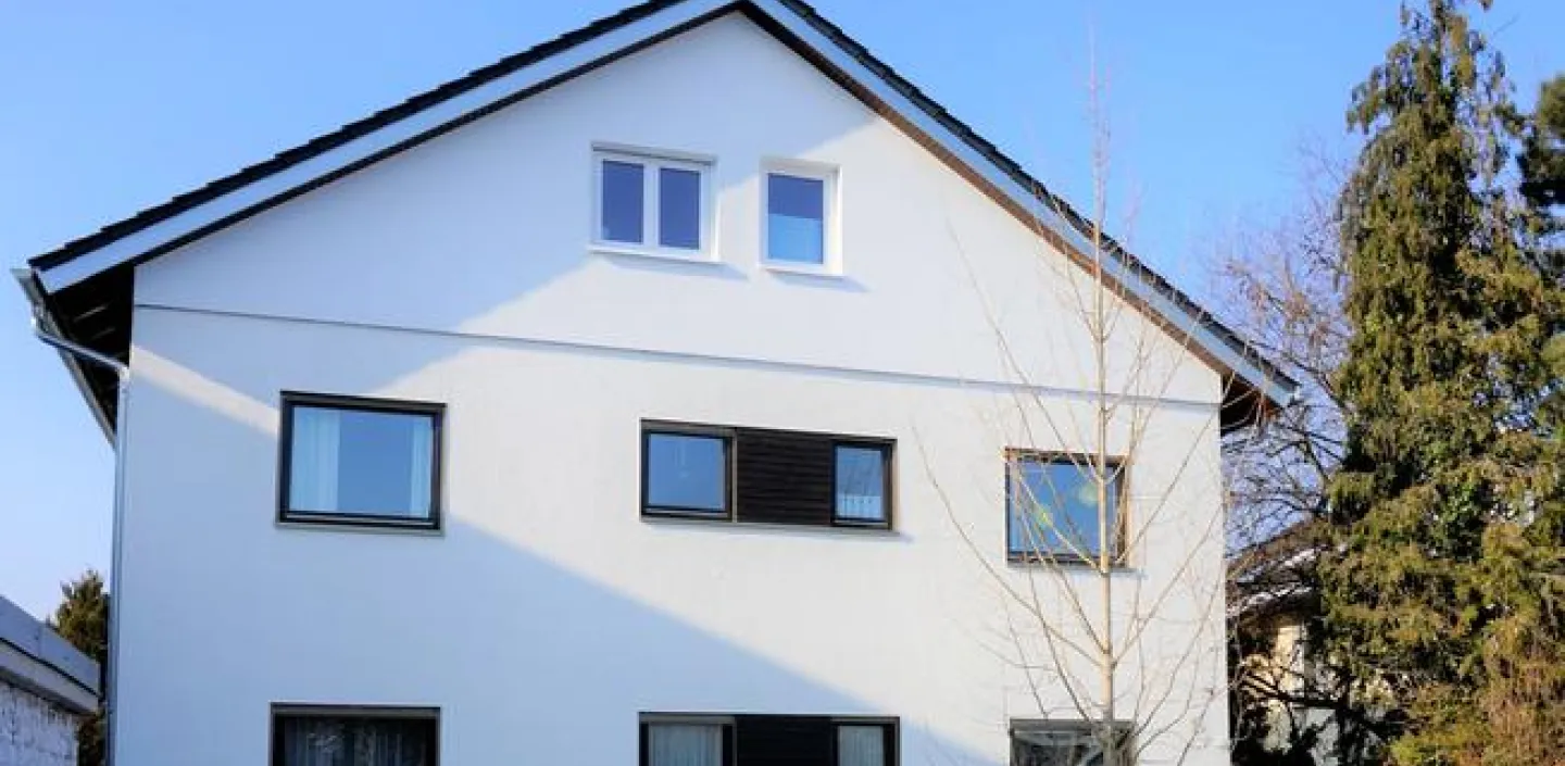 Ein zweistöckiges Einfamilienhaus mit weißer Fassade und schwarzen Fensterrahmen. 