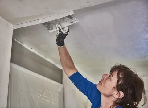 Malerin SHK verputzt Decke eines Baderzimmers.