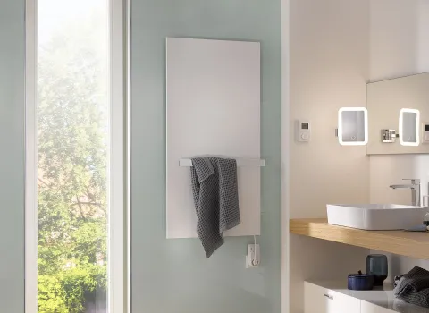 Ein minimalistischer weißer Heizkörper mit Handtuchhalter ist in einem hellen Badezimmer mit Aufsatzwaschbecken und Spiegeln angebracht.