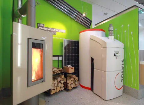 Ein moderner Ausstellungsraum zeigt eine Solvis-Heizung und einen Kaminofen, der mit einem lebendigen Feuer brennt.