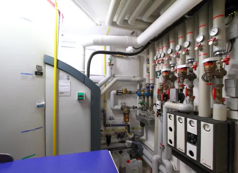 Ein technischer Raum zeigt eine komplexe Heizungsanlage mit mehreren Rohren, Ventilen und Druckanzeigen.