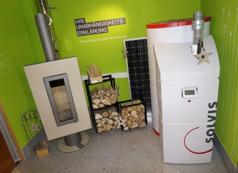 Ein Ausstellungsbereich mit einem modernen Kaminofen, einer Solvis-Heizanlage und einem Solarpanel an der grünen Wand. 