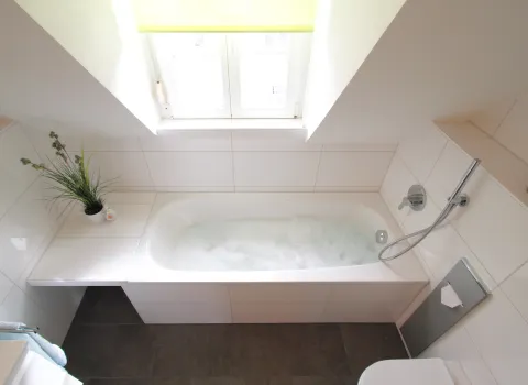 Helle Badezimmeransicht mit einer Badewanne unter einer Dachschräge.
