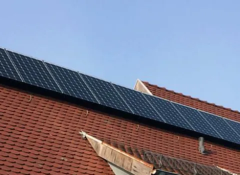 Ein Haus mit schrägem, roten Ziegeldach, auf dem mehrere Solarpanels installiert sind. 