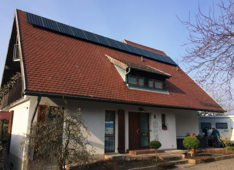 Ein Haus mit schrägem, roten Ziegeldach, auf dem mehrere Solarpanels installiert sind. 