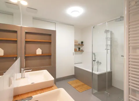 Ein modernes Badezimmer mit Doppelwaschbecken auf einer Holzplatte und großen Spiegeln, die die Raumtiefe betonen.