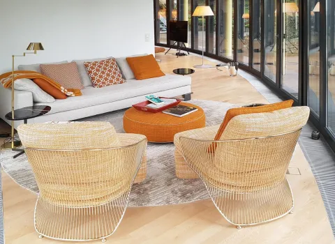 Modern eingerichteter Wintergarten mit großer Fensterfront und gemütlicher Sitzecke. Die Einrichtung kombiniert helle, neutrale Töne mit warmen Akzenten in Orange. Runde Möbel und dezente Dekoration schaffen eine einladende Atmosphäre, ideal für Entspannung und Geselligkeit.