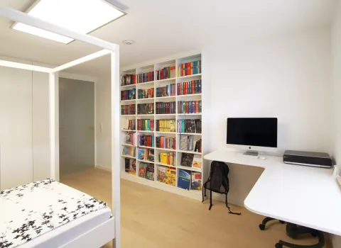 Multifunktionales Arbeits- und Schlafzimmer mit integrierter Bücherwand und modernem Arbeitsplatz, ideal für produktive und erholsame Stunden.