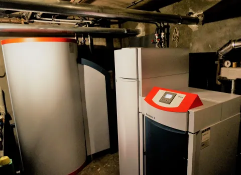 Ein Heizungskeller mit einer modernen Heizungsanlage, bestehend aus einem SolvisLino 3 Heizkessel und einem großen Warmwasserspeicher, umgeben von Rohrleitungen.