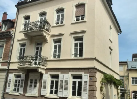 Mehrstöckiges Wohnhaus im klassischen Stil mit dekorativen Balkonen und Fensterläden, an einer ruhigen Straße gelegen.