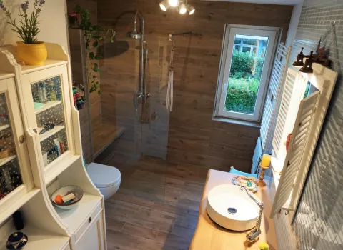 Ein stilvolles Badezimmer mit einer großen bodengleichen Dusche, deren Rückwand in Holzoptik gestaltet ist. 