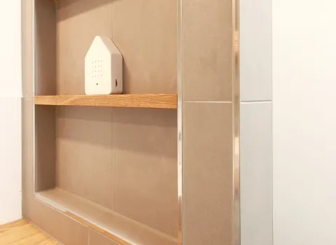 Detailaufnahme eines eingebauten Regals mit Holzablage in einem modernen Badezimmer. Dezente Dekoration, darunter ein kleines Accessoire in Hausform, unterstreicht das minimalistische Design.