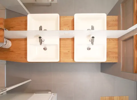 Doppelwaschtisch mit weißer Keramik und einer Arbeitsplatte aus hellem Holz, aufgenommen aus der Vogelperspektive. Moderne Armaturen und klare Linien sorgen für ein harmonisches und funktionales Design.
