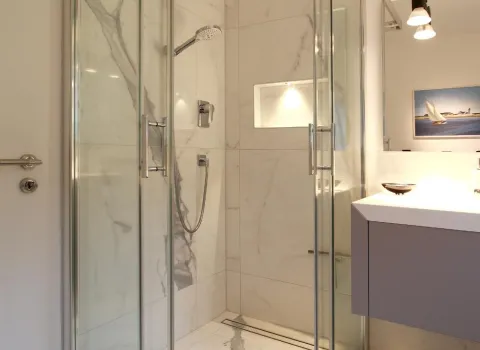 Eine luxuriöse Duschkabine mit Marmoreffekt-Fliesen und einer Schiebetür aus klarem Glas.