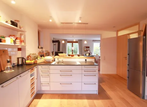 Eine offene Wohnküche mit einer zentralen Kücheninsel, weißen Schränken und dunklen Arbeitsplatten. 