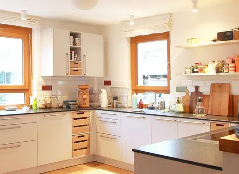 Eine helle, moderne Küche mit weißen Schränken und einer dunklen Arbeitsplatte, die U-förmig angeordnet ist.