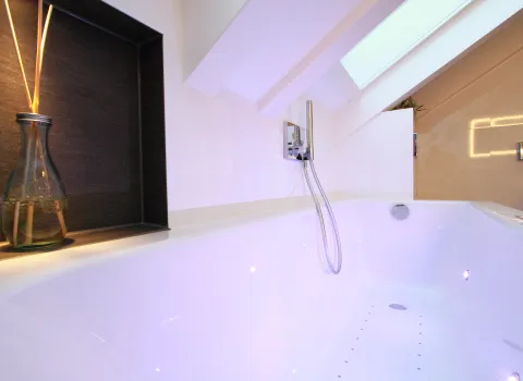 Ein luxuriöses Badezimmer mit einer freistehenden weißen Badewanne, die unter einer schrägen Decke platziert ist. 