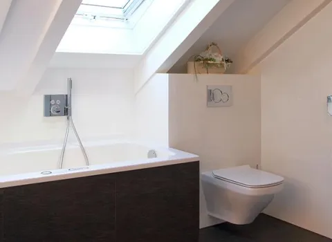 Ein modernes Badezimmer unter einer Dachschräge mit einer großzügigen Badewanne und einem Fenster, das Tageslicht hereinlässt.