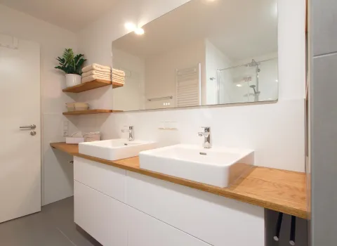 Modernes Badezimmer mit Doppelwaschtisch, Holzarbeitsplatte und großzügigem Spiegel. 