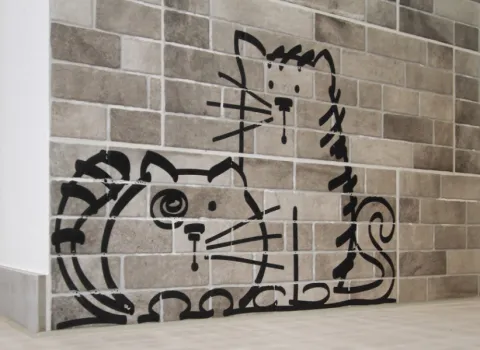 Eine dekorative Wand aus braunen Mosaikfliesen mit einem aufgemalten Katzenmotiv in schwarzer Linienzeichnung.