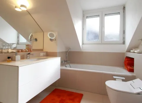 Ein modernes Badezimmer unter einer Dachschräge mit beige-weißen Fliesen und einer hellen, freundlichen Gestaltung.