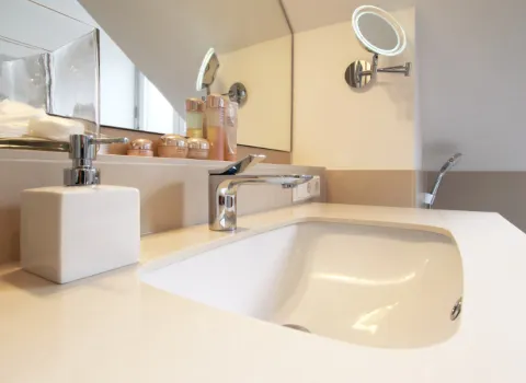 Nahaufnahme eines modernen Waschbeckens mit einer glatten weißen Oberfläche und einem eleganten Chrom-Wasserhahn. 