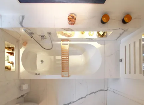 Draufsicht auf eine moderne Badewanne aus Marmor mit integrierten, beleuchteten Wandnischen, dekorativen Accessoires und einem Handtuchhalter mit türkisfarbenem Handtuch an der Wand.