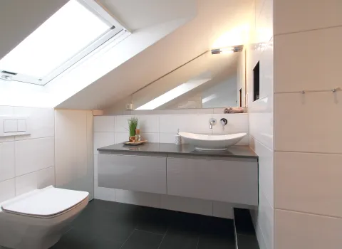 Ein modernes Badezimmer unter einer Dachschräge mit einem großen Dachfenster, das viel Tageslicht hereinlässt. 