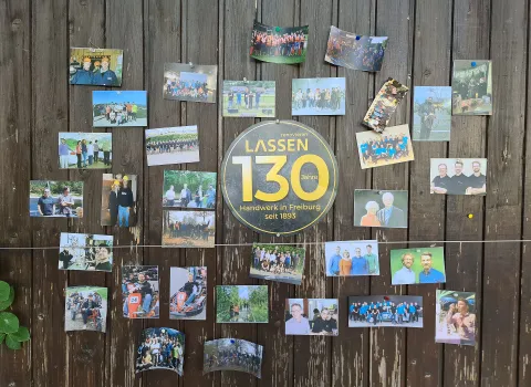 An einer rustikalen Holzwand sind zahlreiche Fotos angebracht, die das langjährige Bestehen und die Tradition eines Handwerksunternehmens dokumentieren.