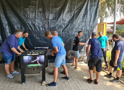 Mehrere Personen stehen bei einem Teamevent um einen Tischkicker und spielen in lockerer Atmosphäre.