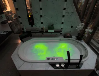 Ein luxuriöser Whirlpool in einem modernen Badezimmer, dessen Wasser in grüner LED-Beleuchtung schimmert. 