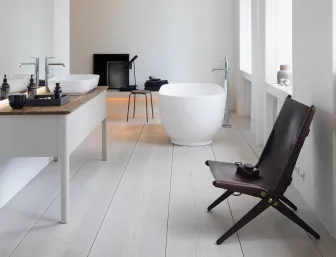 Ein geräumiges, minimalistisches Badezimmer mit einer freistehenden, ovalen Badewanne und einem Waschbecken auf einer Holzarbeitsplatte. 